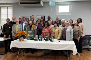 Ajené with a group of the book's contributing authors and editors, standing behind a table of books.