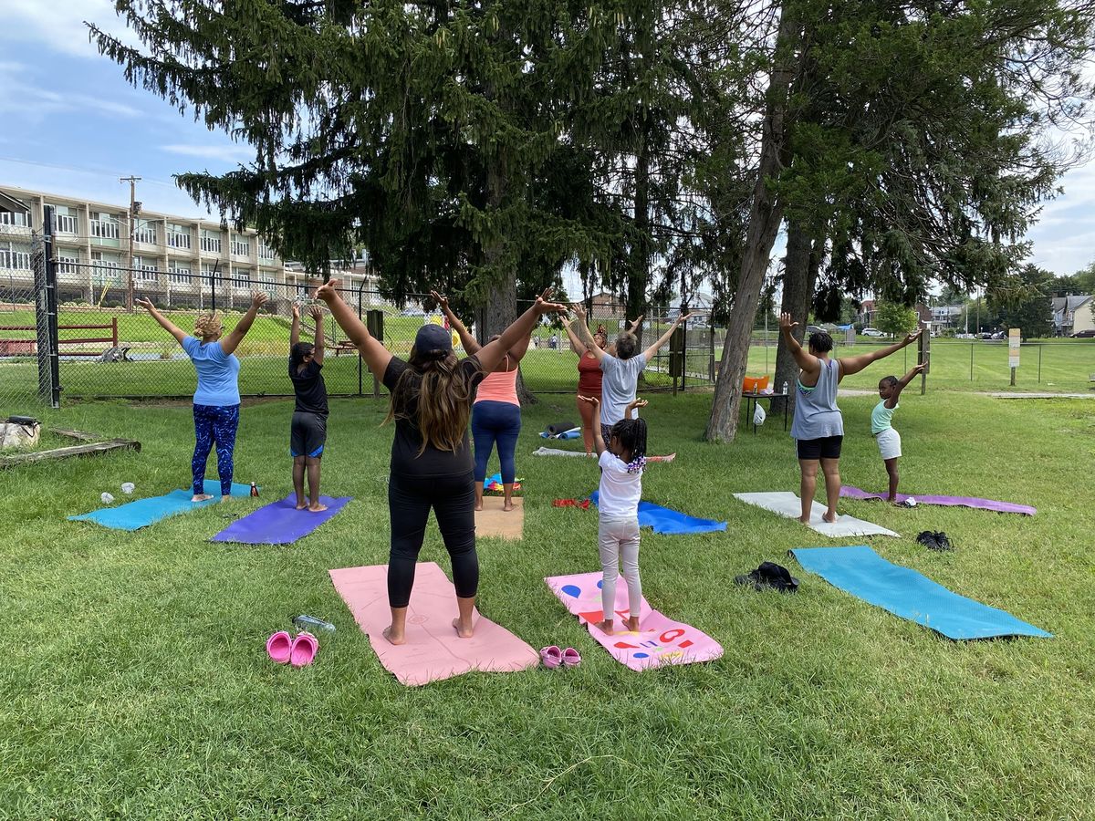 Families doing yoga together on colorful mats under tall evergreens at Sundays in the Park in Coatesville.